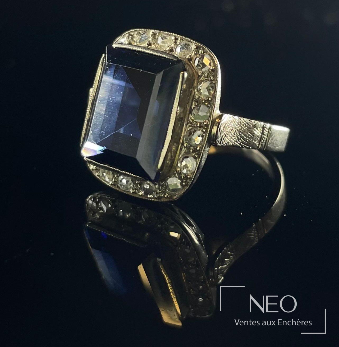 Bague cocktail en or gris avec pierre bleue rectangulaire et entourage de diamants sur fond noir