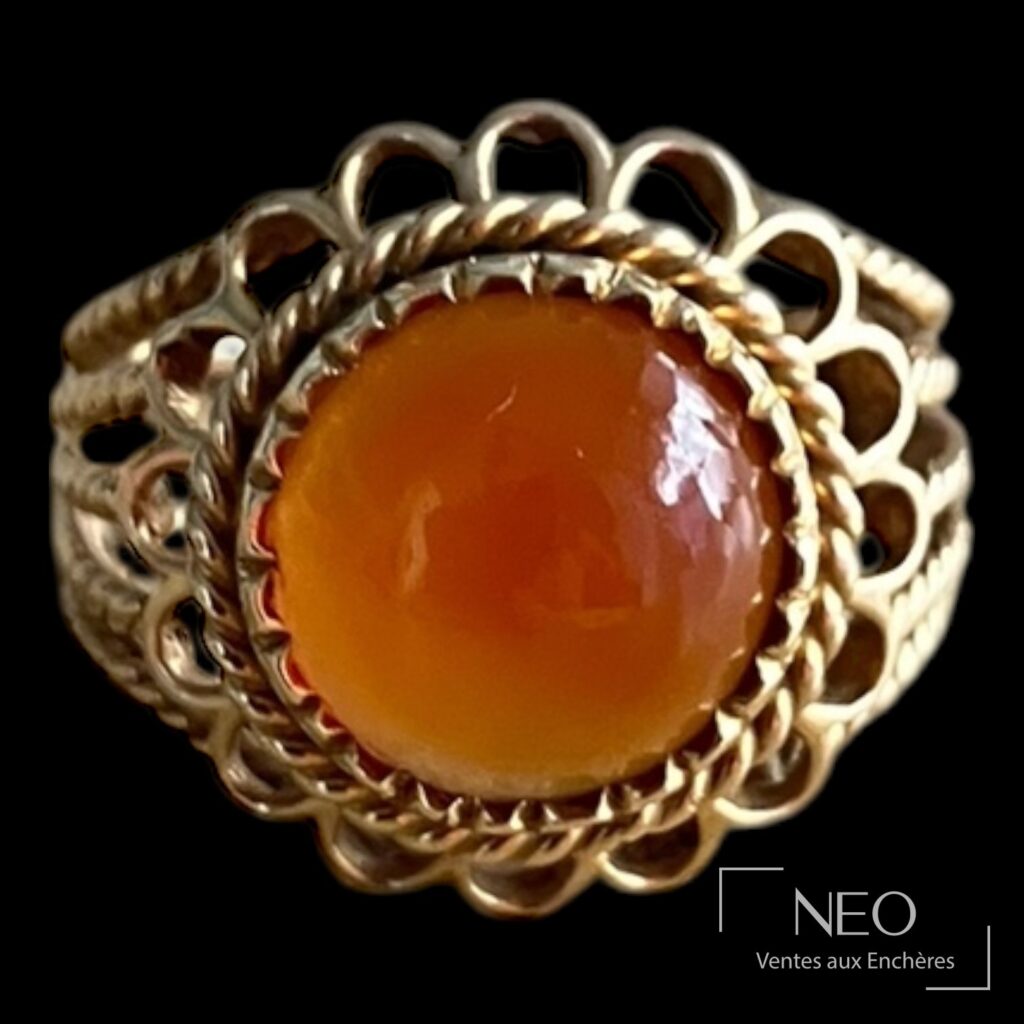 Bague dôme en or jaune avec cabochon orange centré sur un fond noir