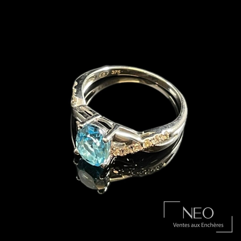 Bague en or blanc sertie d'une pierre bleue et de petites pierres blanches sur fond noir