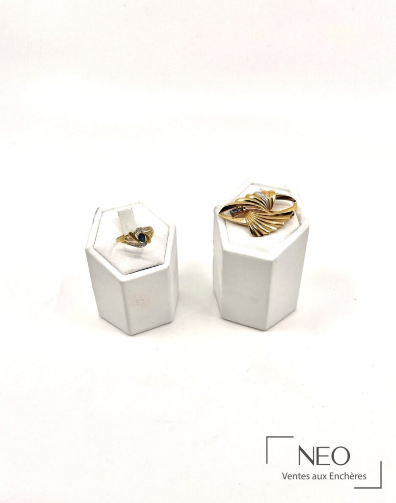 Bague en or jaune et broche dorée présentées sur deux supports blancs