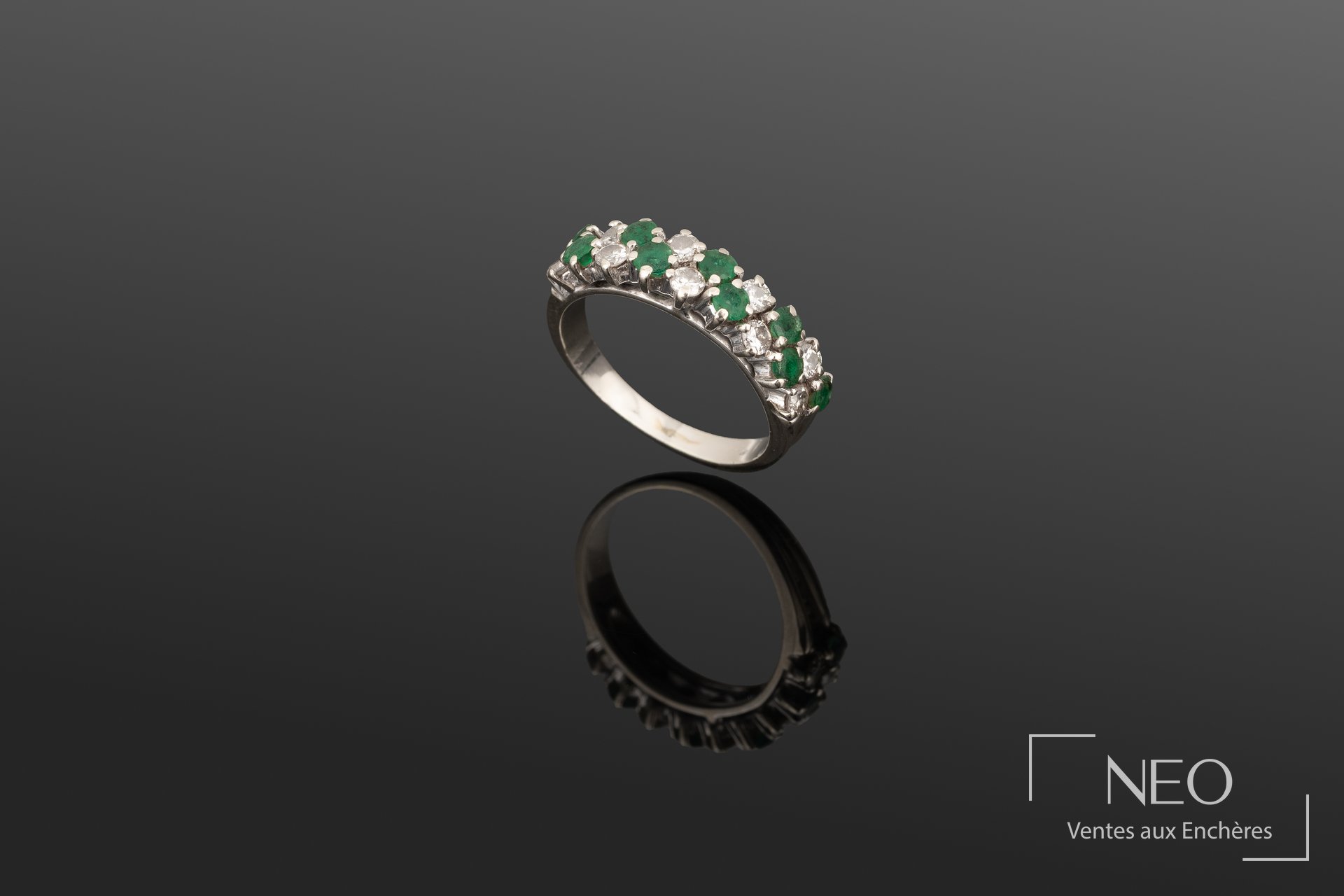 Bague en or gris ornée de diamants ronds et d'émeraudes rondes sur fond sombre