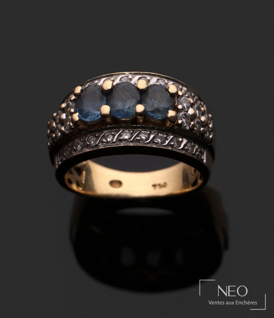 Bague en or gris et or jaune sertie de trois pierres bleues et de diamants sur fond sombre