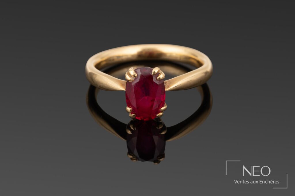 Bague en or jaune sertie d'une pierre rouge ovale sur fond gris