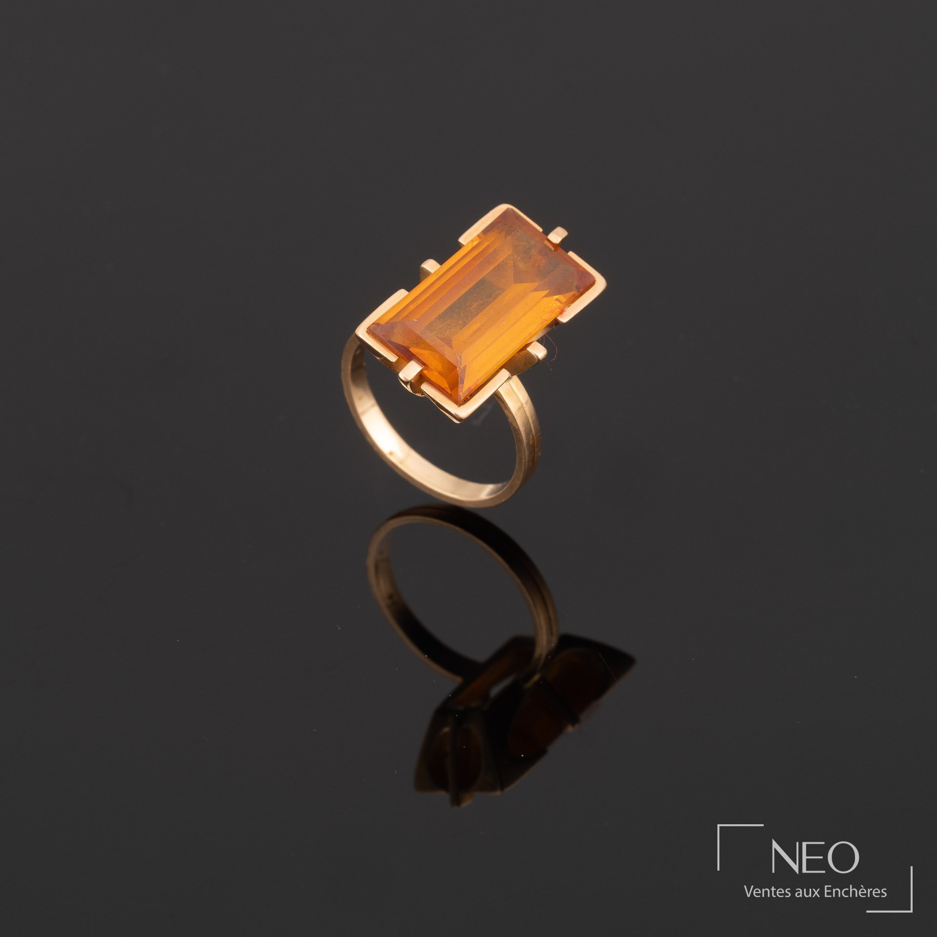 Bague en or jaune sertie d’une pierre orange rectangulaire sur fond noir
