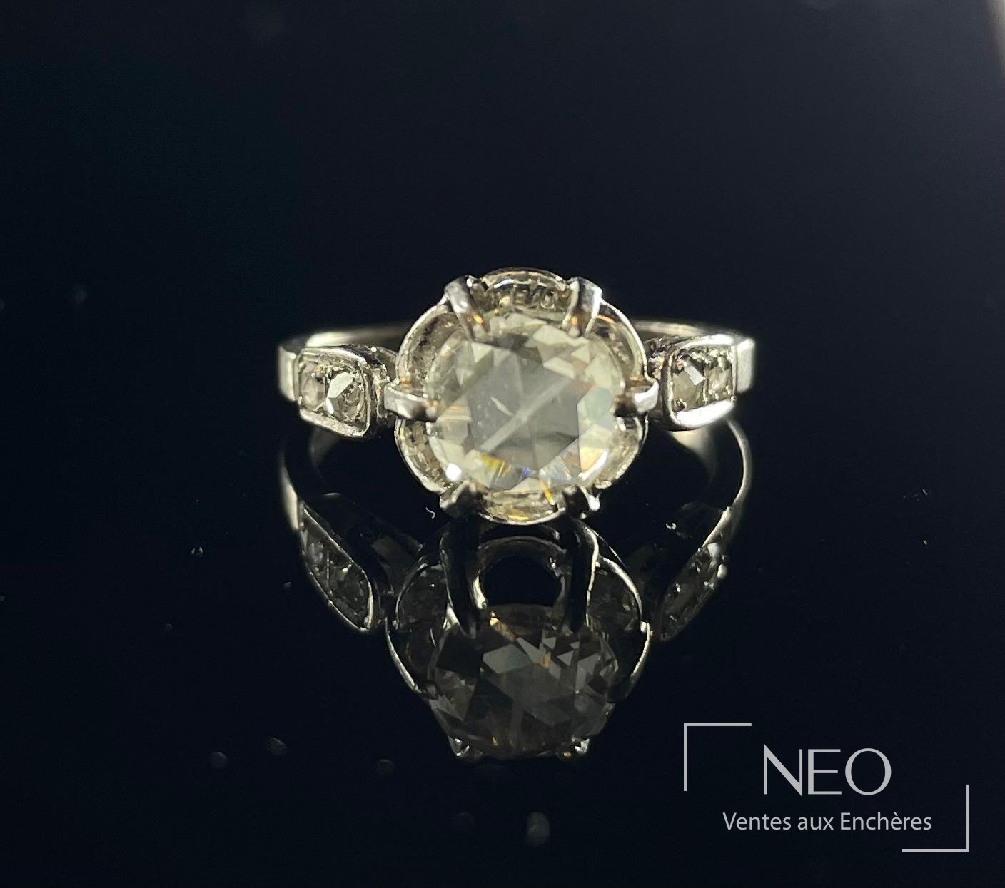 Bague solitaire en or gris avec diamant central et petits diamants latéraux sur fond noir