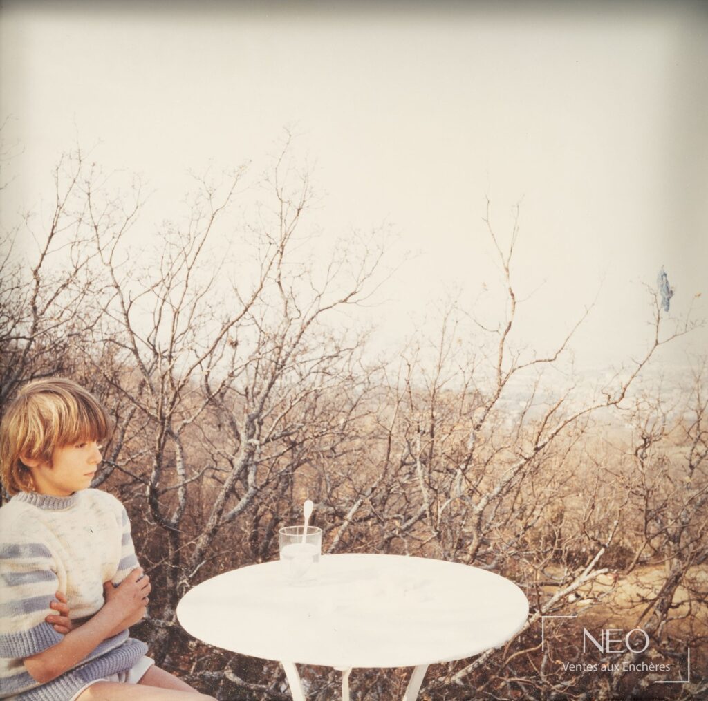 Photographie de Bernard Faucon montrant un enfant assis près d'une table blanche avec un verre d'eau sucrée