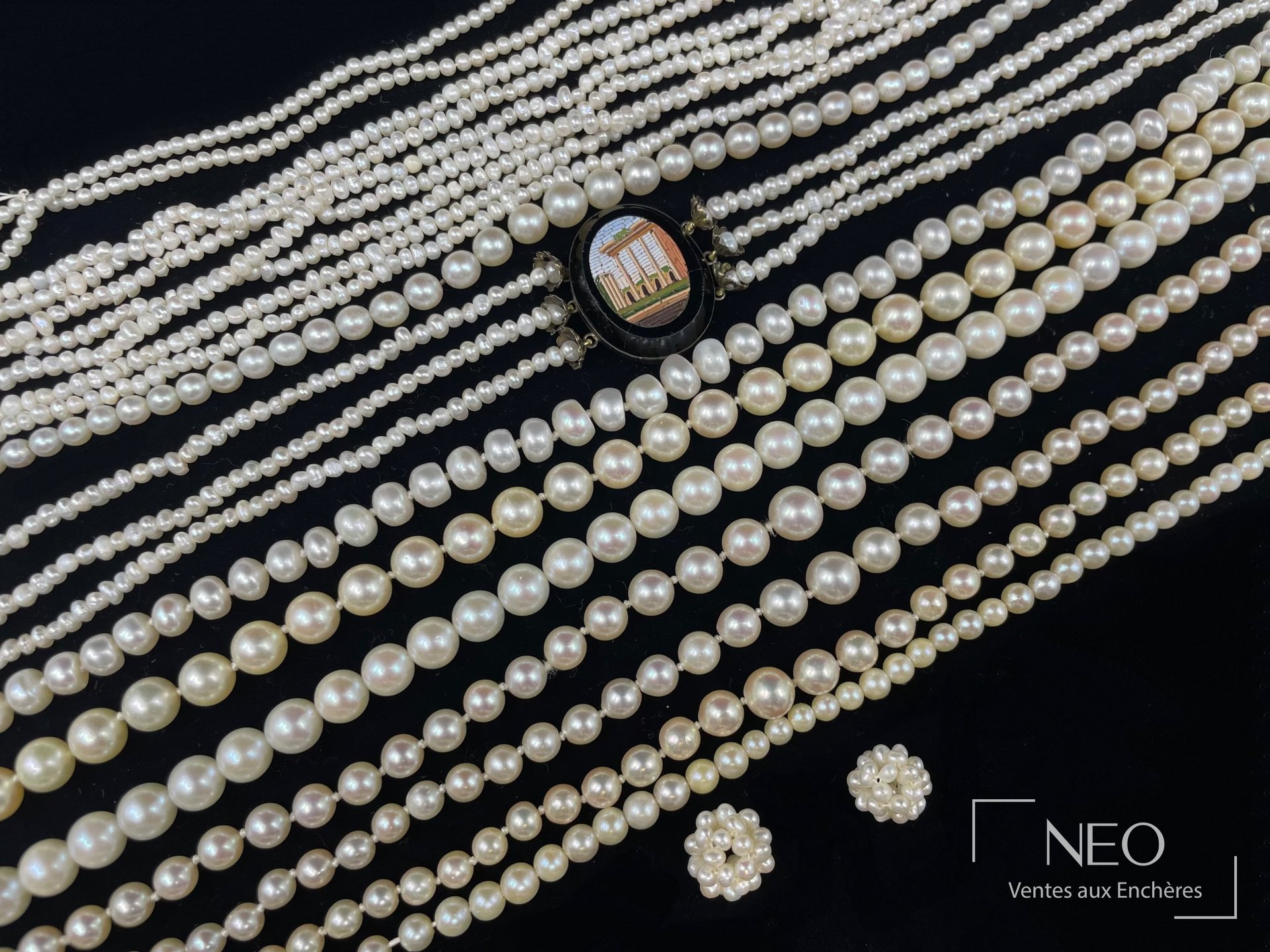 Plusieurs colliers de perles de culture blanches disposés sur fond noir