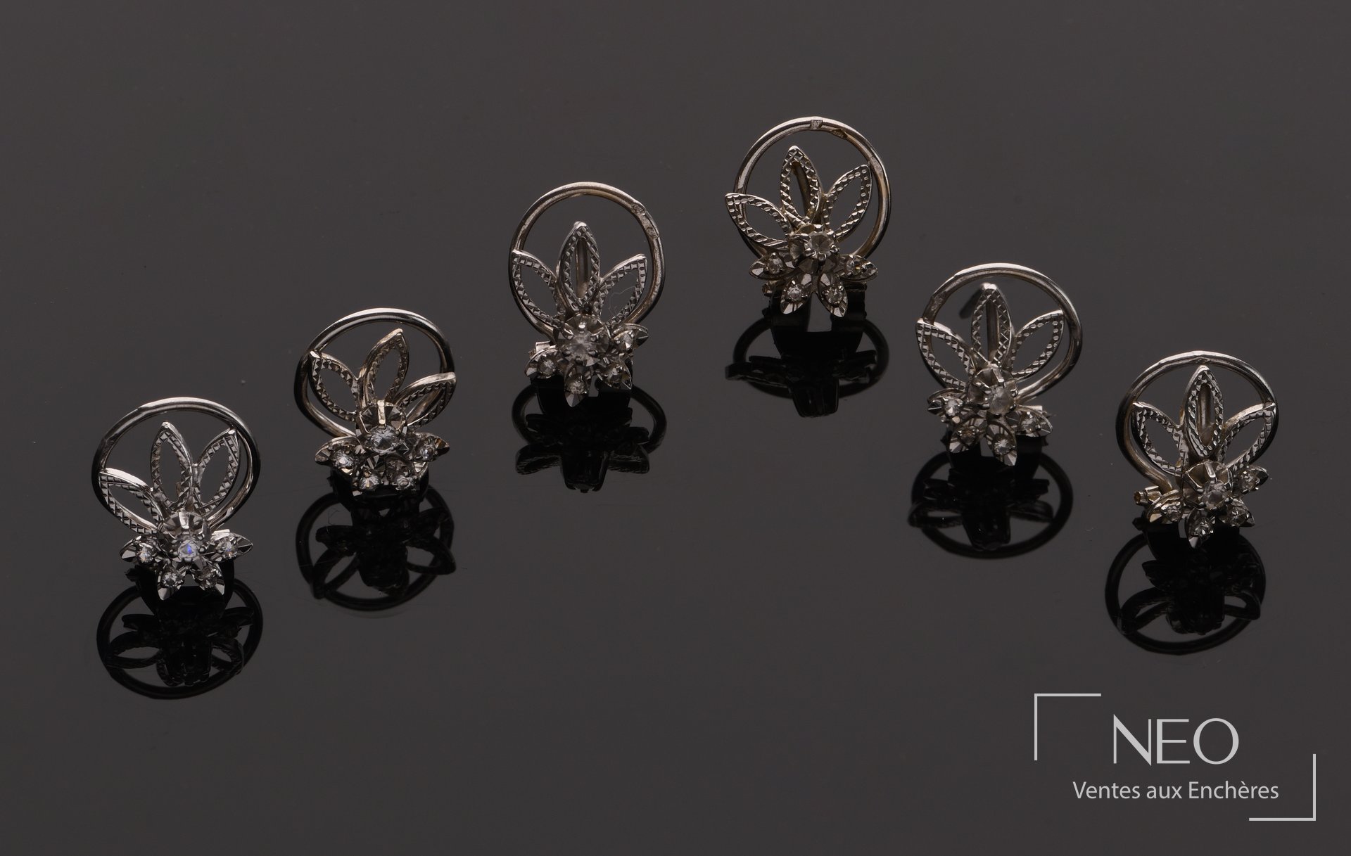 Six boucles d'oreille en or gris et diamants présentées sur fond sombre