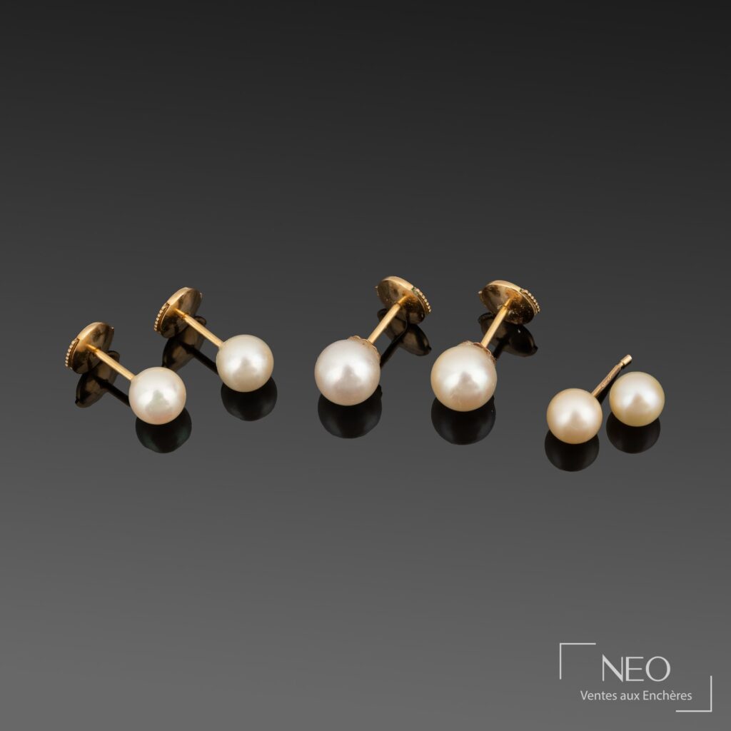 Cinq boucles d’oreilles à perles de culture blanches posées en ligne sur fond sombre