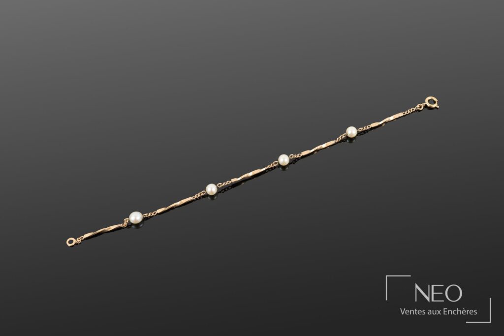 Bracelet en or jaune avec maillons torsadés et perles blanches sur fond gris