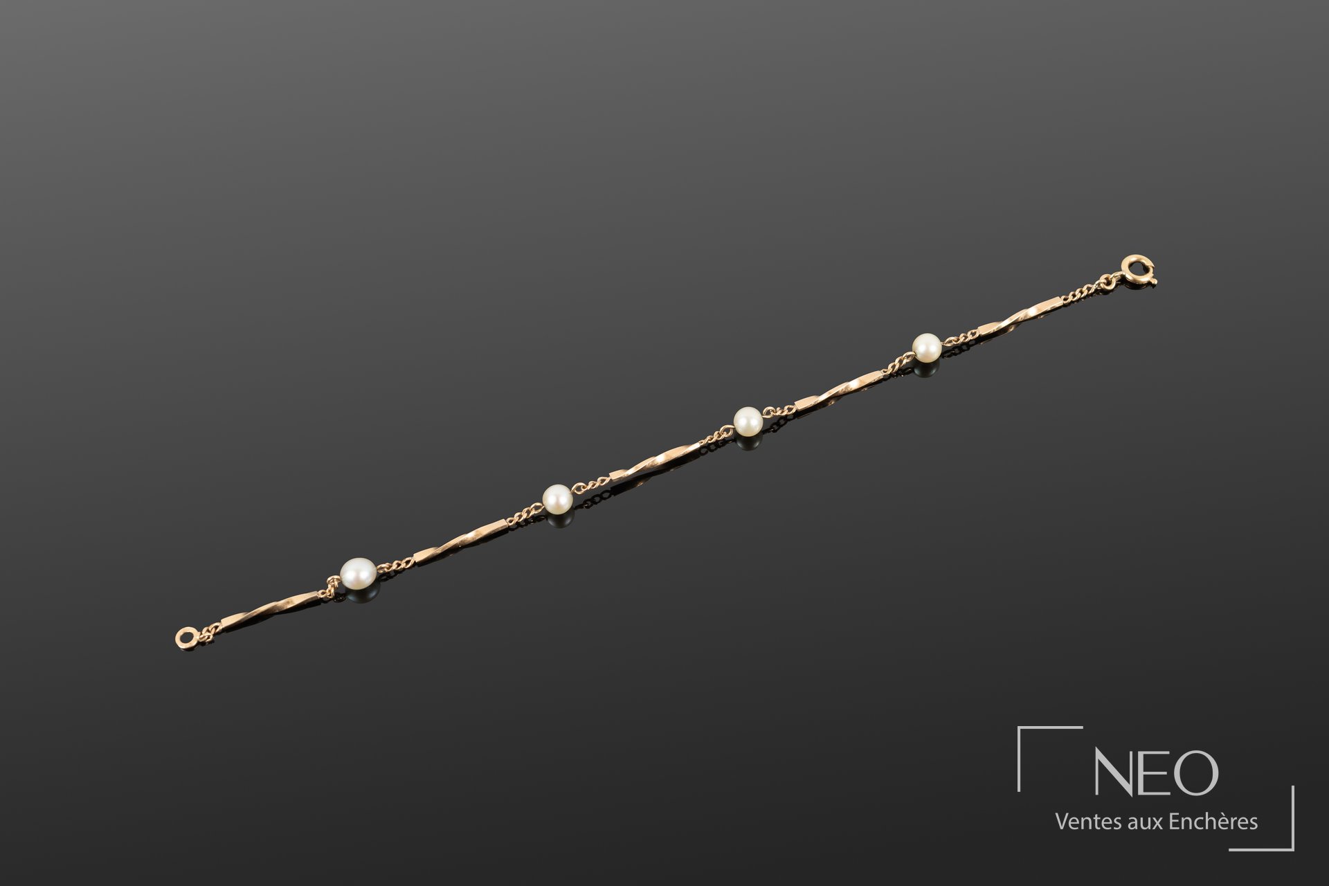 Bracelet en or jaune avec maillons torsadés et perles blanches sur fond gris
