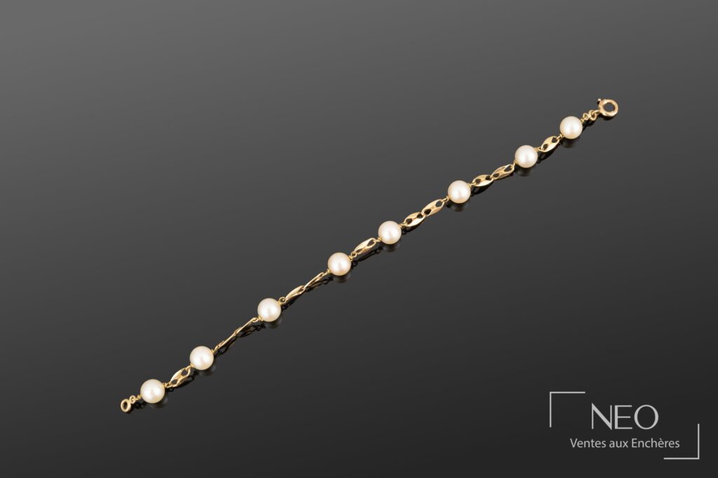 Bracelet en or jaune avec perles de culture blanches et maillons ajourés sur fond gris