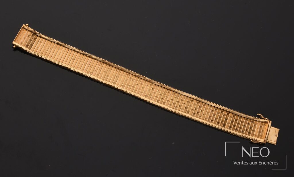 Bracelet manchette en or jaune à mailles verticales articulées sur fond noir