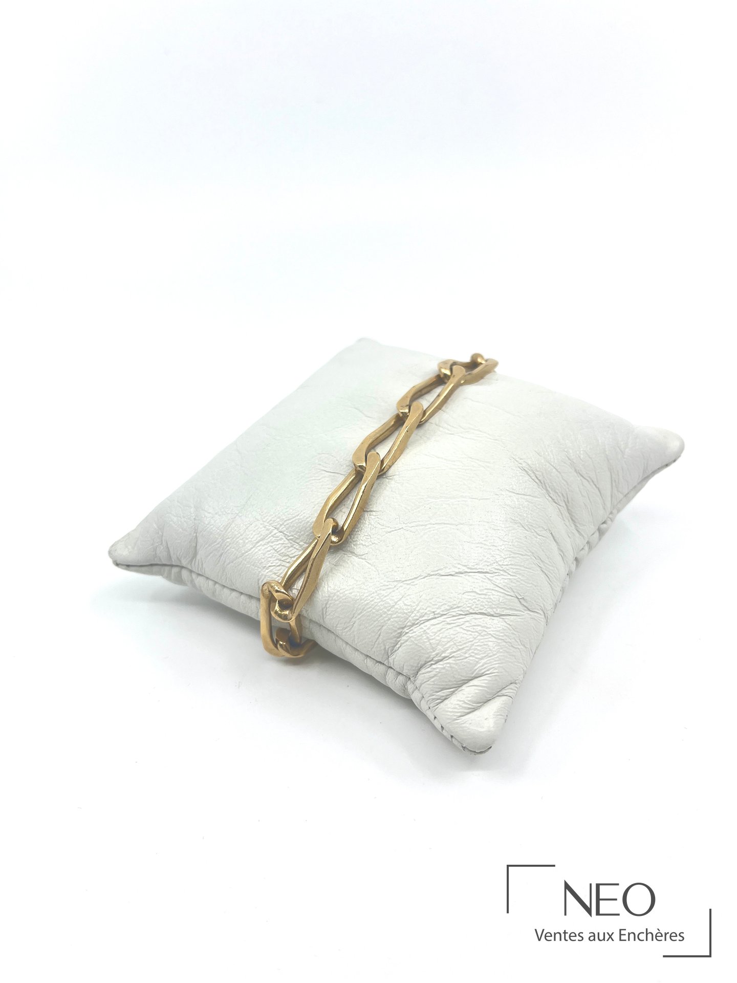 Bracelet en or jaune à mailles allongées posé en diagonale sur un coussin blanc