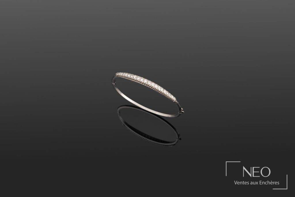 Bracelet rigide ouvrant en or blanc serti d'une ligne de diamants sur fond sombre