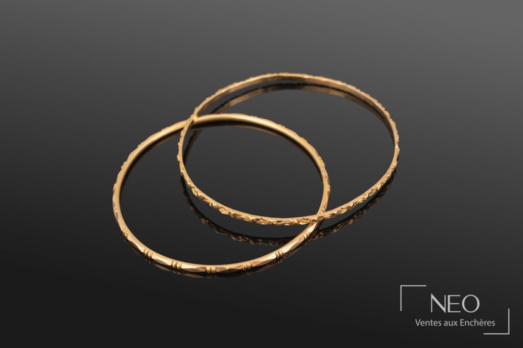 Deux bracelets jonc en or jaune posés en superposition sur fond noir