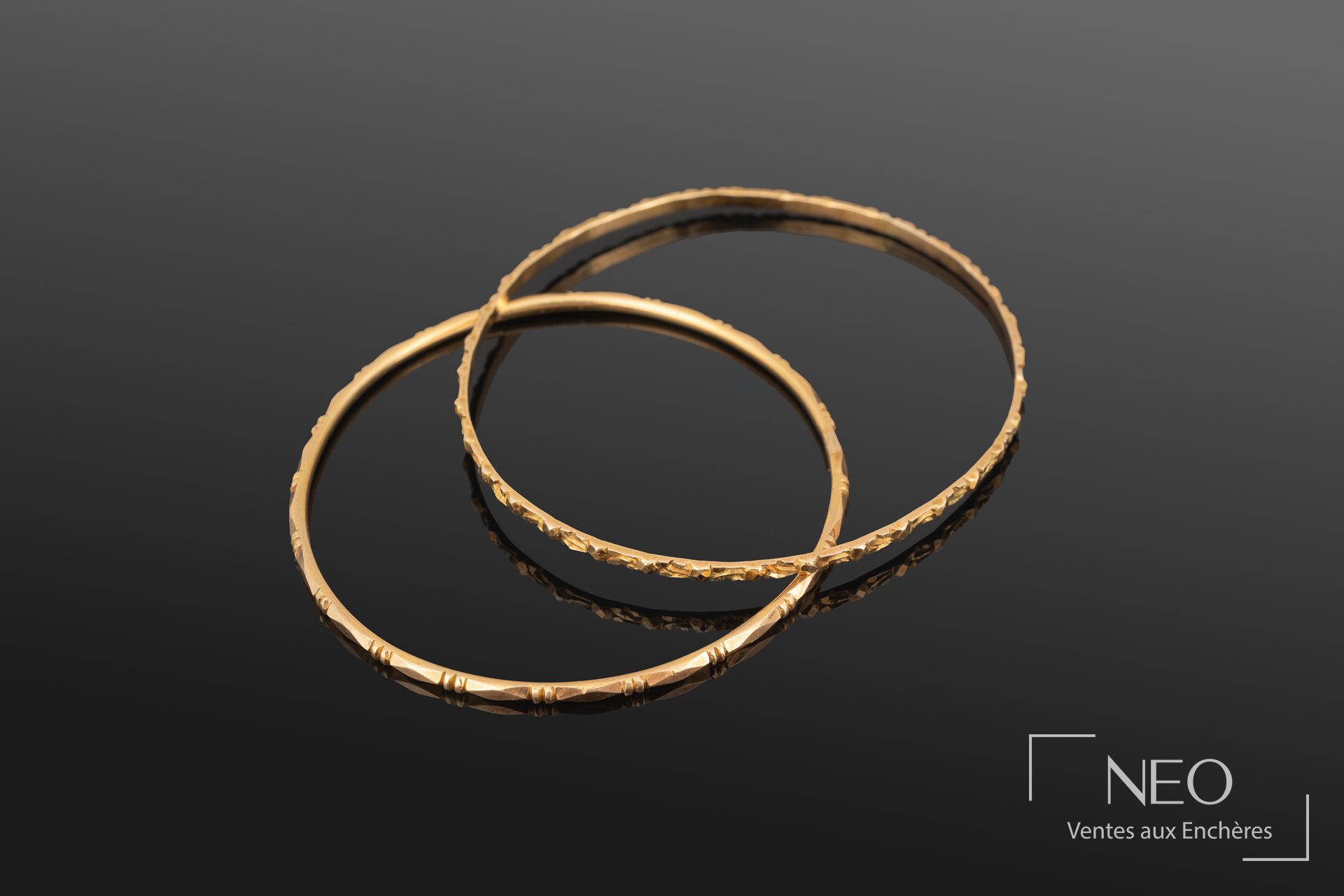 Deux bracelets jonc en or jaune posés en superposition sur fond noir