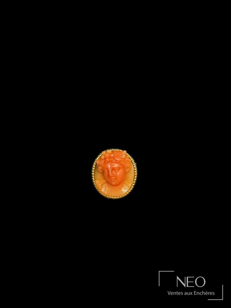Broche ronde en or jaune ornée d'un visage féminin en corail rouge sur fond noir