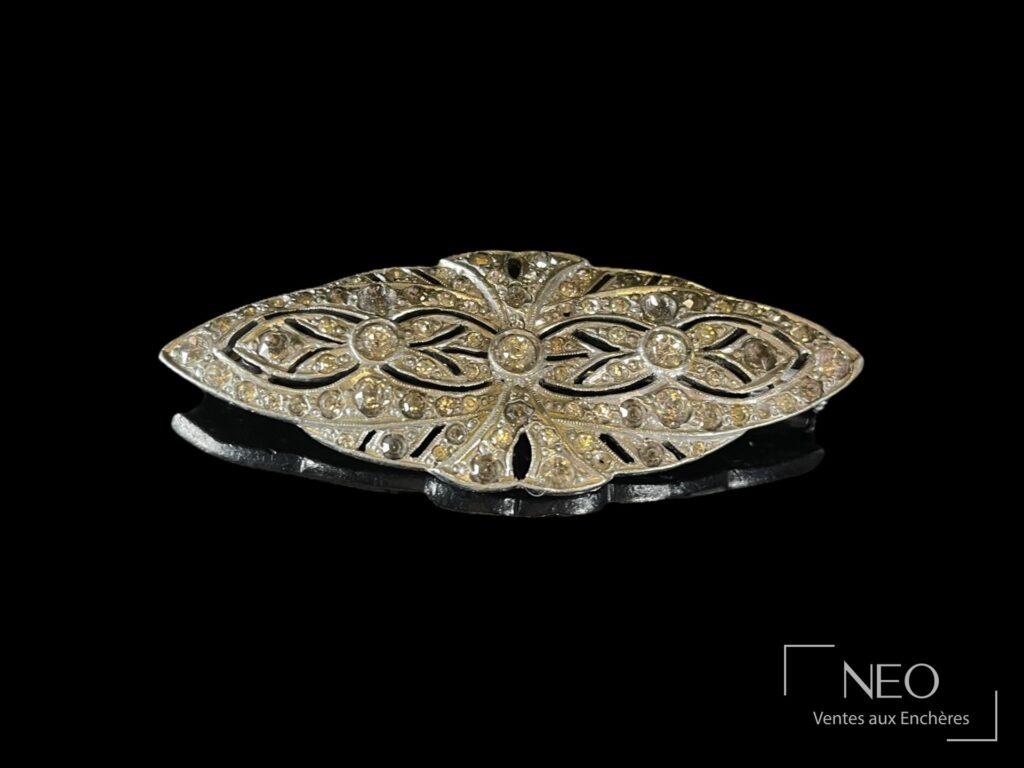 Broche losange en métal ajouré sertie de pierres blanches sur fond noir