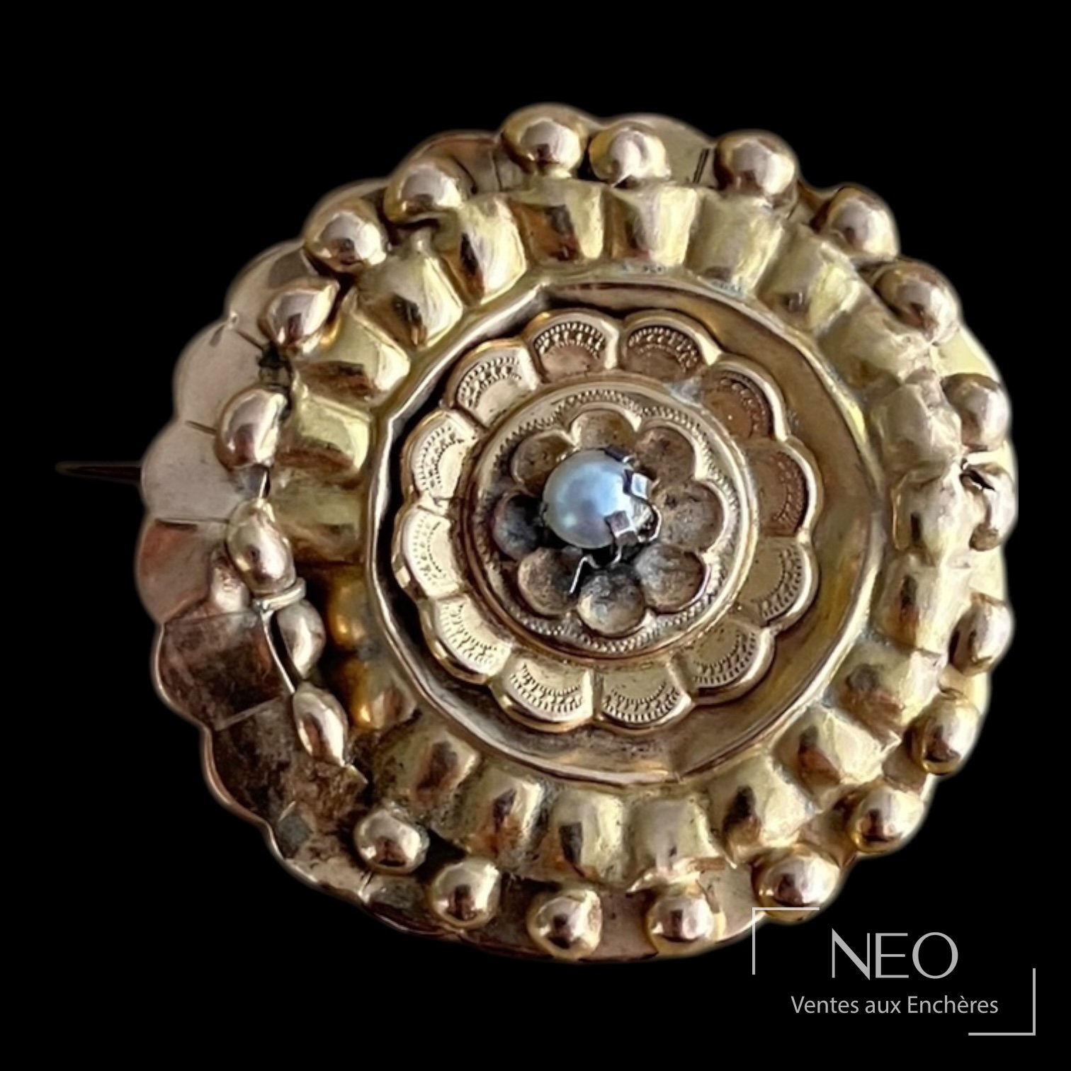 Broche circulaire en or rose avec perle blanche centrale sur fond noir