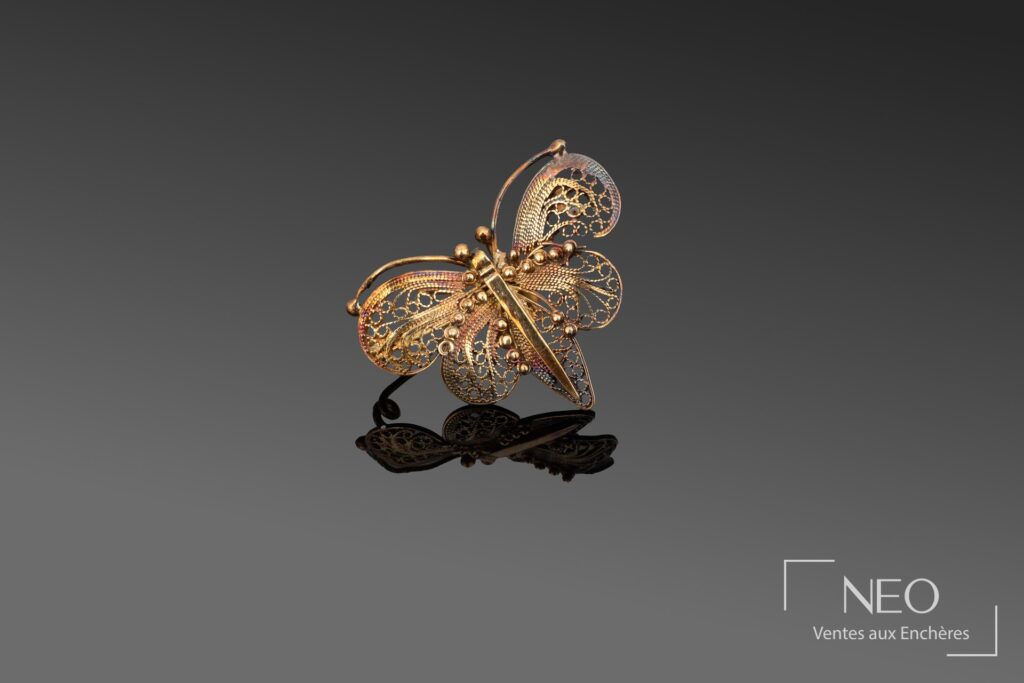 Broche papillon en or jaune ajouré sur fond gris