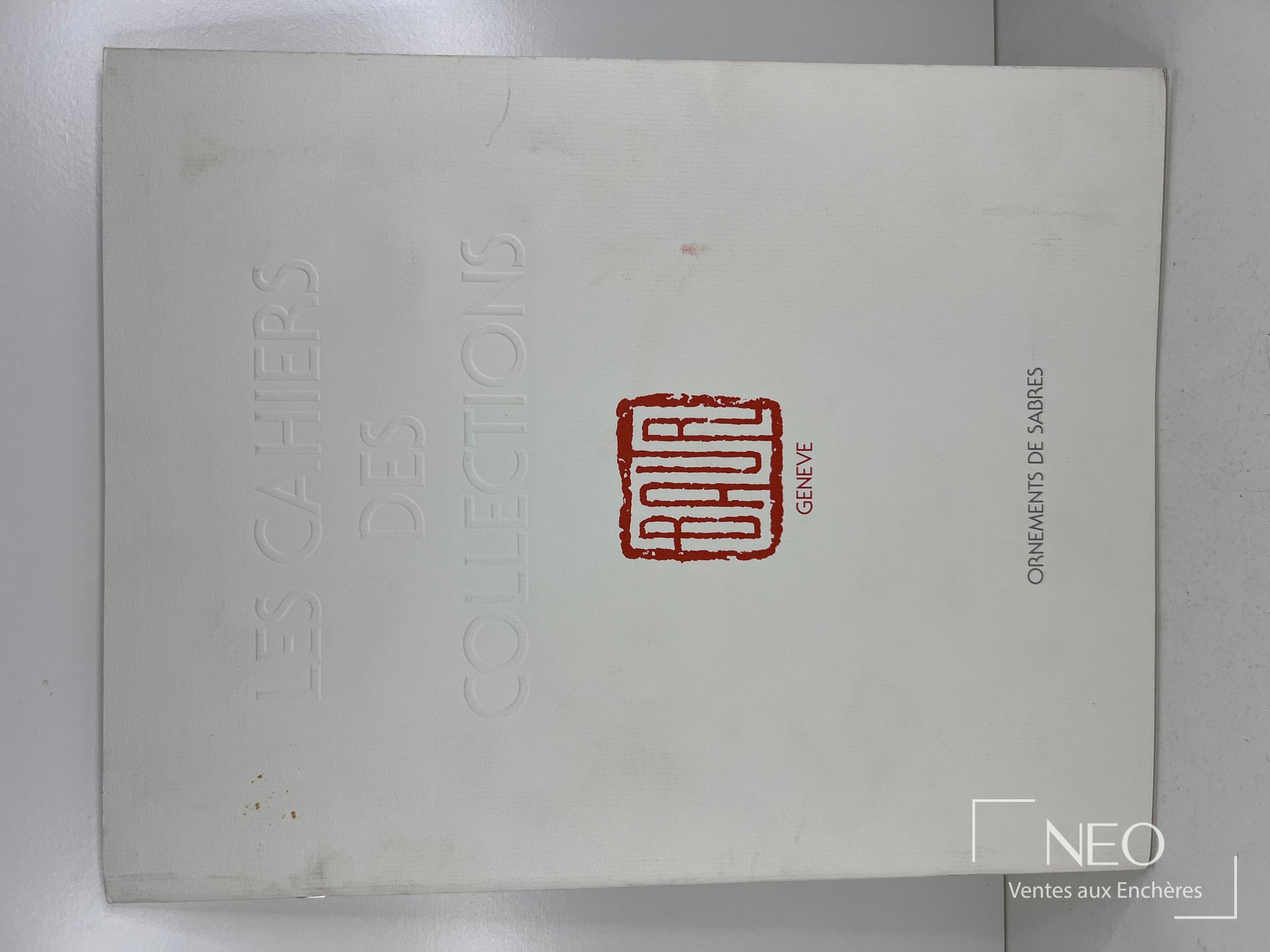 Couverture blanche du cahier Les cahiers des collections Baur avec titre en relief et logo rouge.