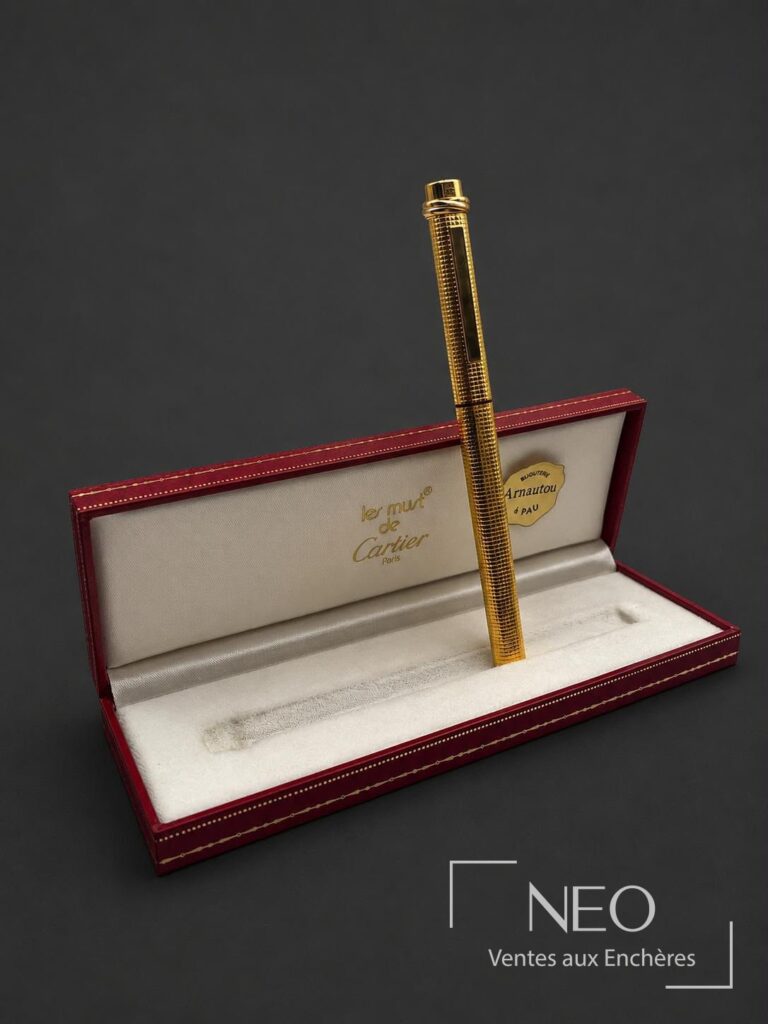 Stylo-bille Cartier doré présenté dans son écrin rouge et beige
