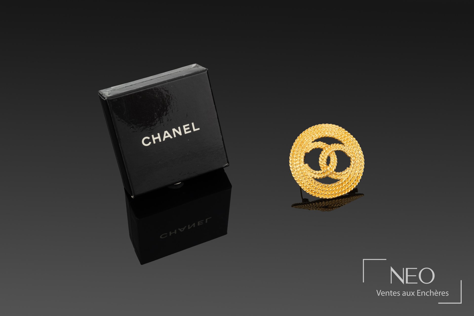 Broche circulaire Chanel en métal doré avec boîte noire siglée
