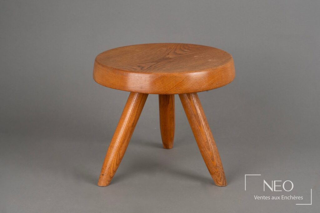 Tabouret bas en frêne à assise circulaire et trois pieds visibles sur fond gris