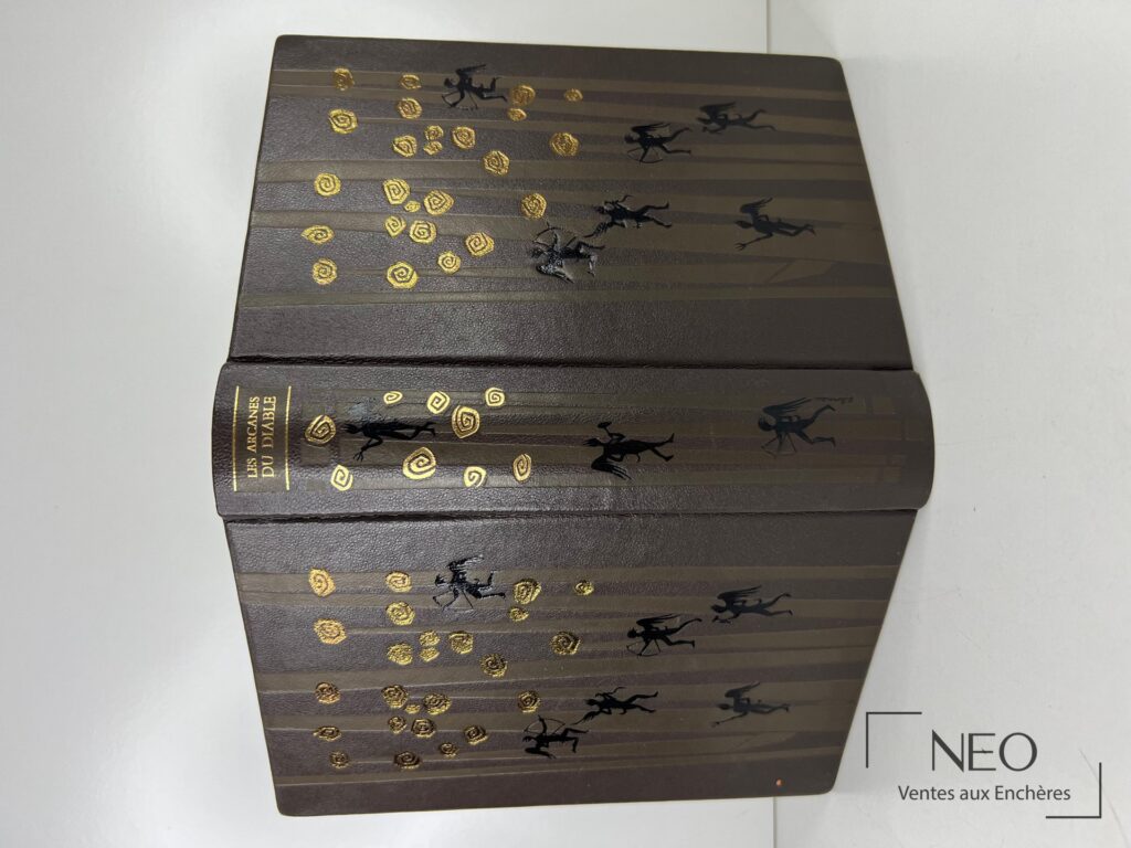 Livre relié sombre orné de motifs dorés et de silhouettes noires sur les plats