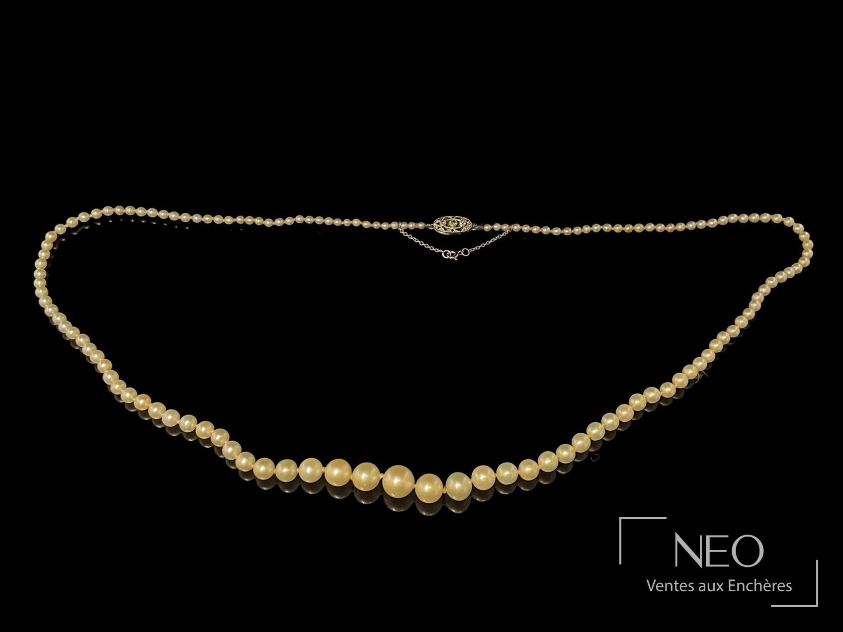 Collier de perles blanches en chute avec fermoir central et chaîne de sécurité sur fond noir