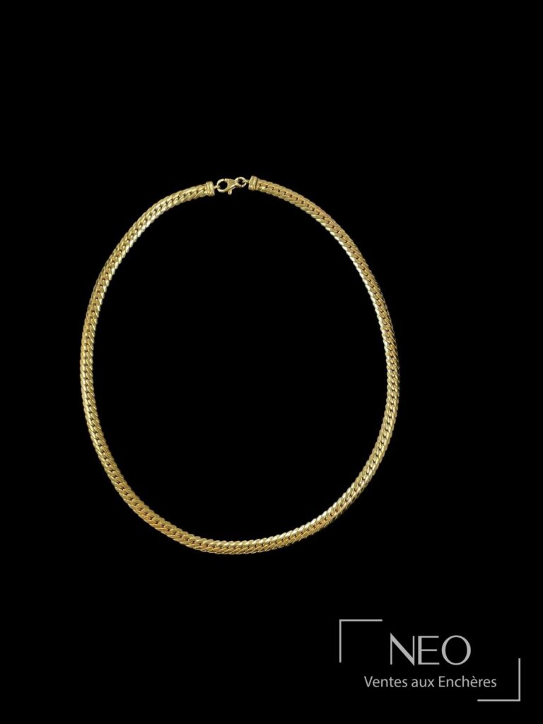 Collier en or jaune à mailles anglaises sur fond noir.