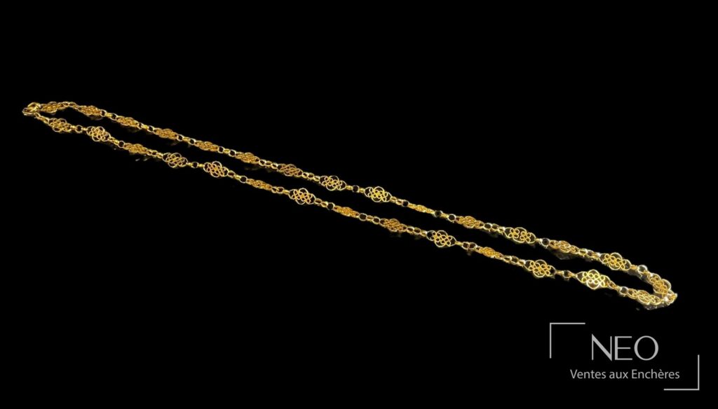Collier en or jaune à mailles filigrannées posé sur fond noir