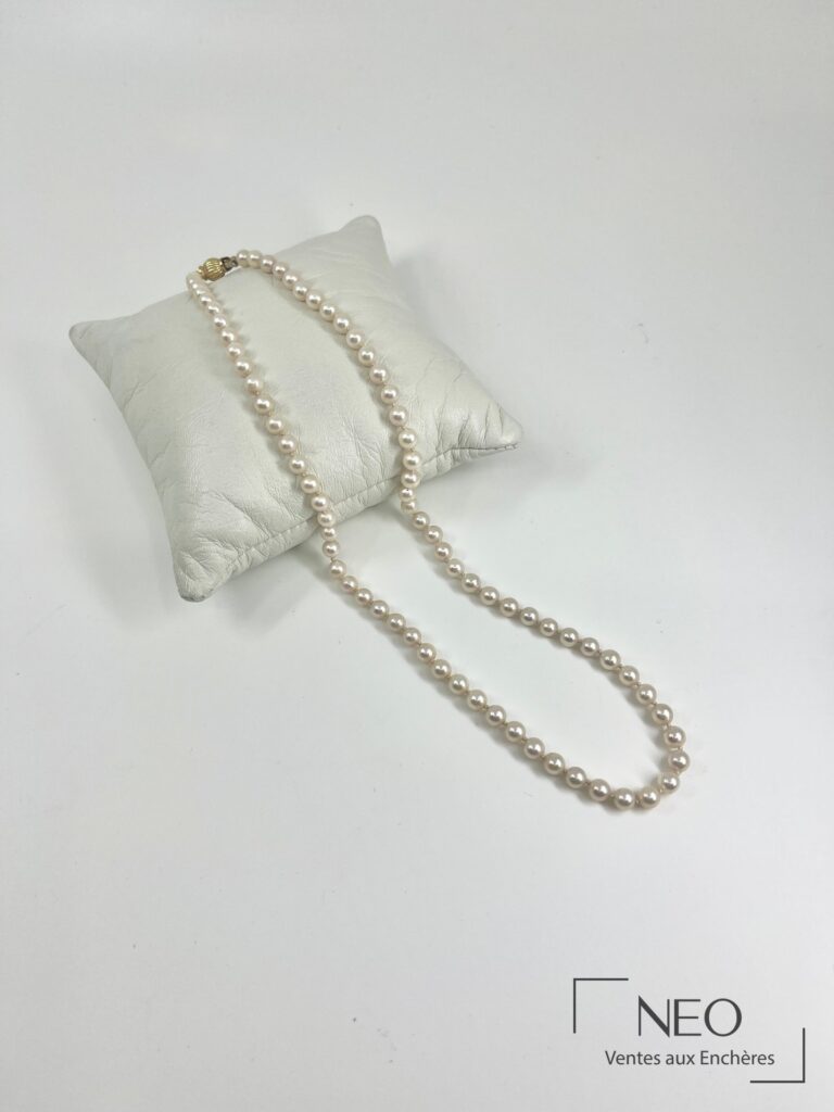 Collier ras de cou en perles de culture avec fermoir doré posé sur un coussin blanc