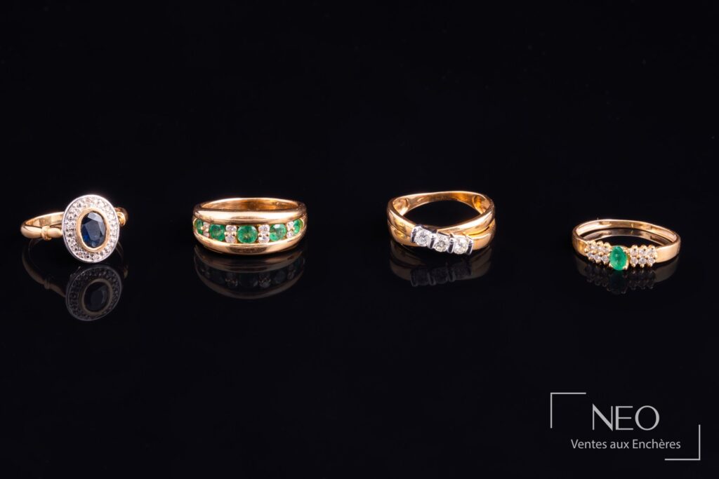 Quatre bagues en or serties de diamants et de pierres de couleur alignées sur fond noir