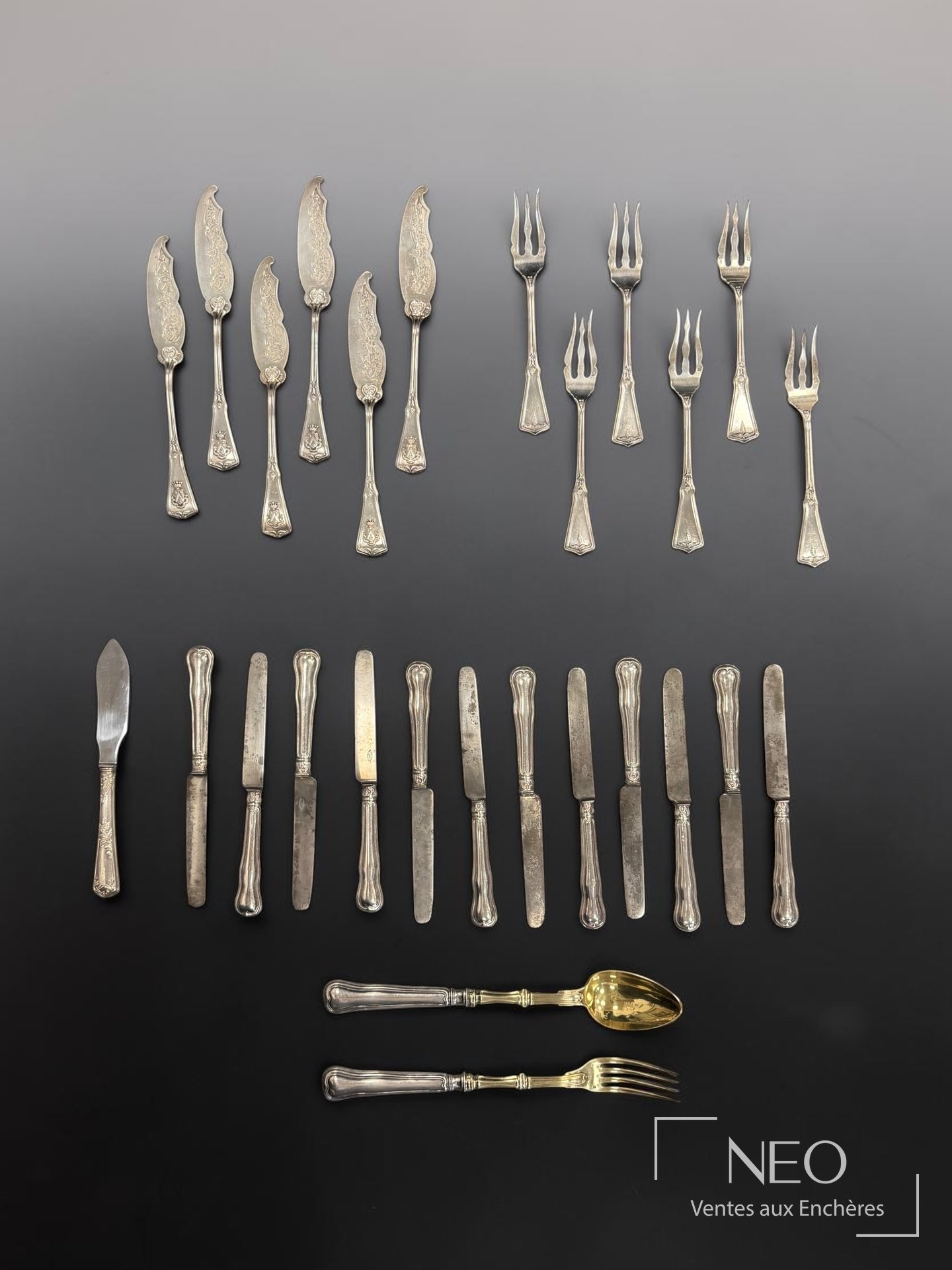 Ensemble de couverts en argent et métal argenté disposés en rangées sur fond noir et gris