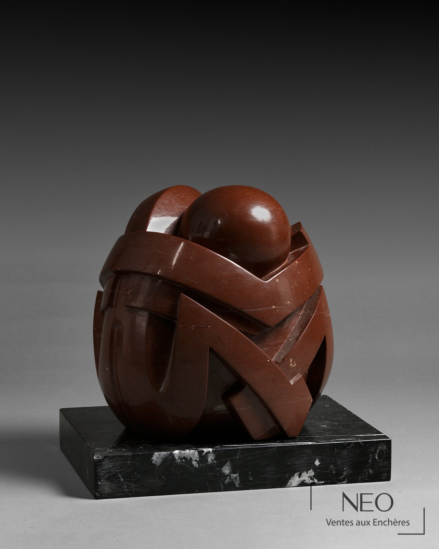 Sculpture abstraite en porphyre rouge posée sur un socle en marbre noir veiné blanc
