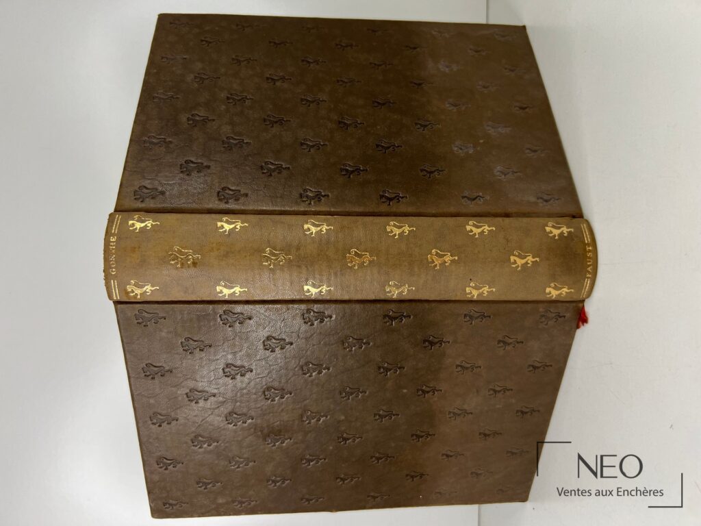 Livre relié brun avec dos lisse décoré de motifs dorés et titre en lettres dorées