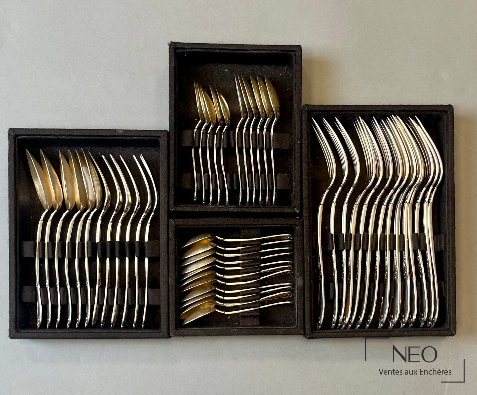 Quatre boîtes noires présentant des fourchettes et cuillères en argent disposées à plat