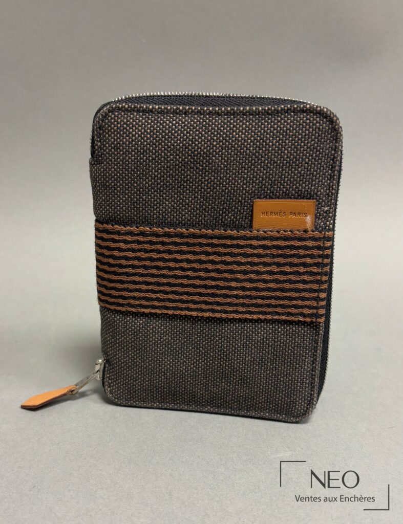 Portefeuille Hermès en toile sombre avec bande à motifs vagues orange et tirette en cuir.