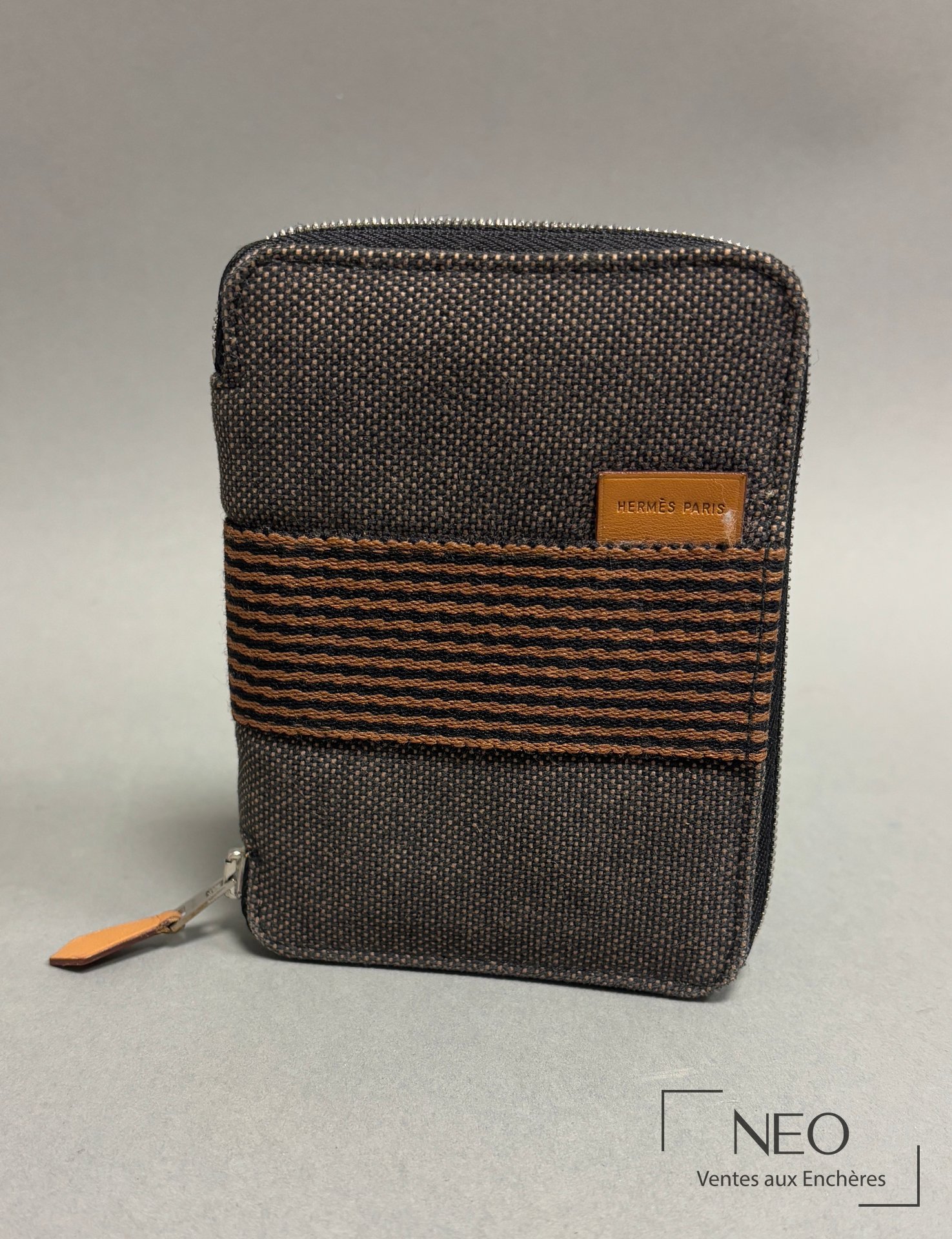 Portefeuille Hermès en toile sombre avec bande à motifs vagues orange et tirette en cuir.
