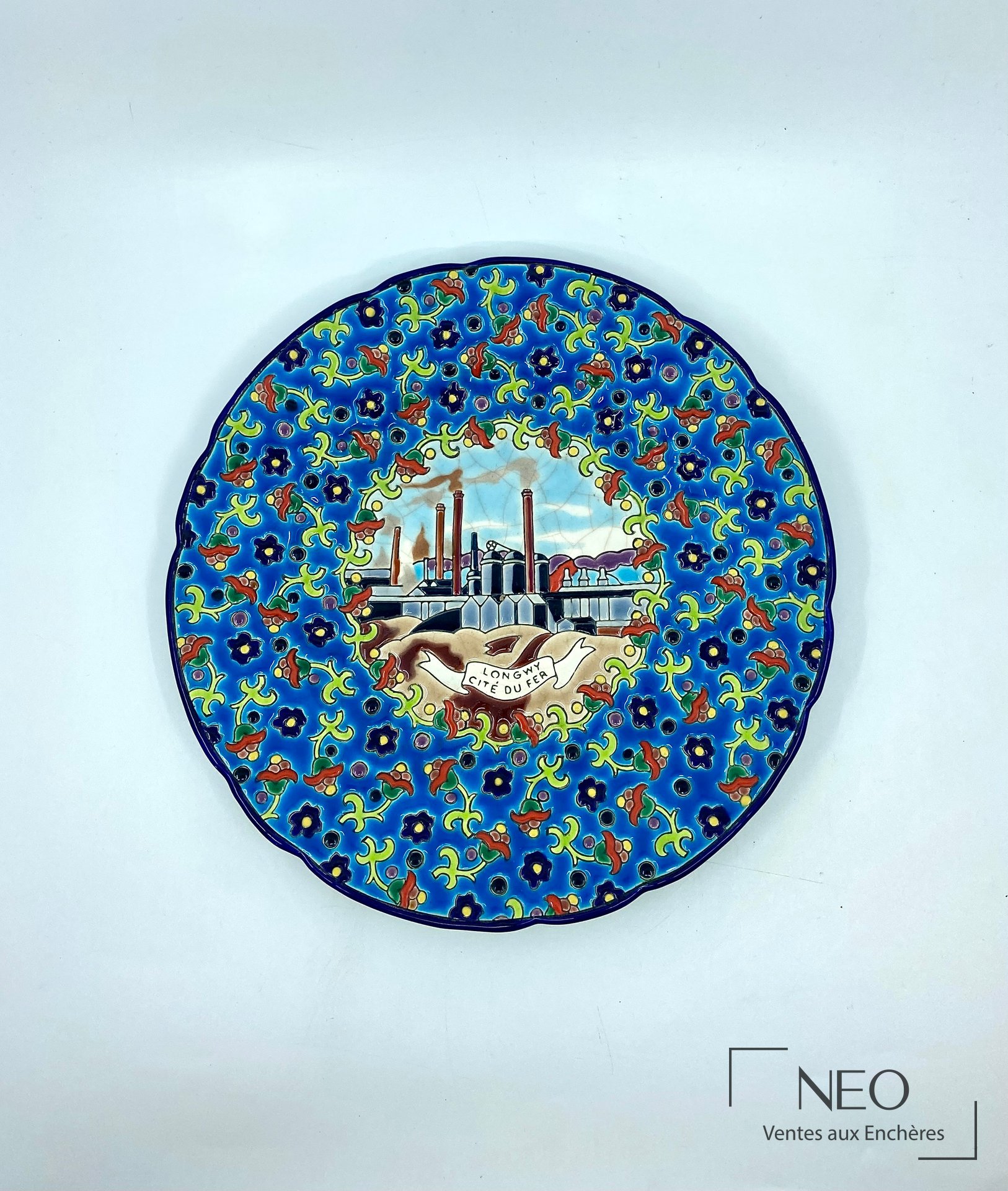 Assiette Longwy en émaux polychromes à décor floral et médaillon central industriel