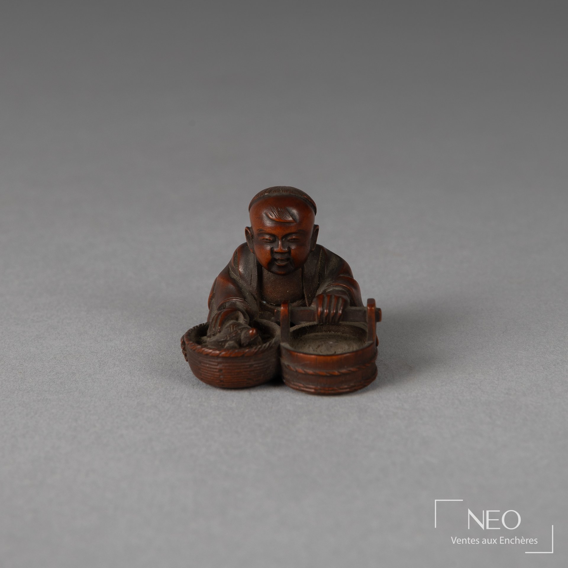 Netsuke japonais en buis représentant un enfant assis près de deux baquets tenant une tortue