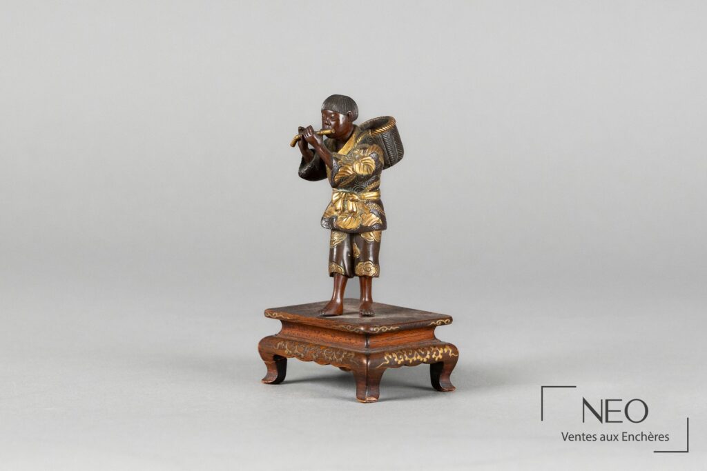 Okimono japonais en bronze représentant un joueur de flûte sur socle en bois décoré.