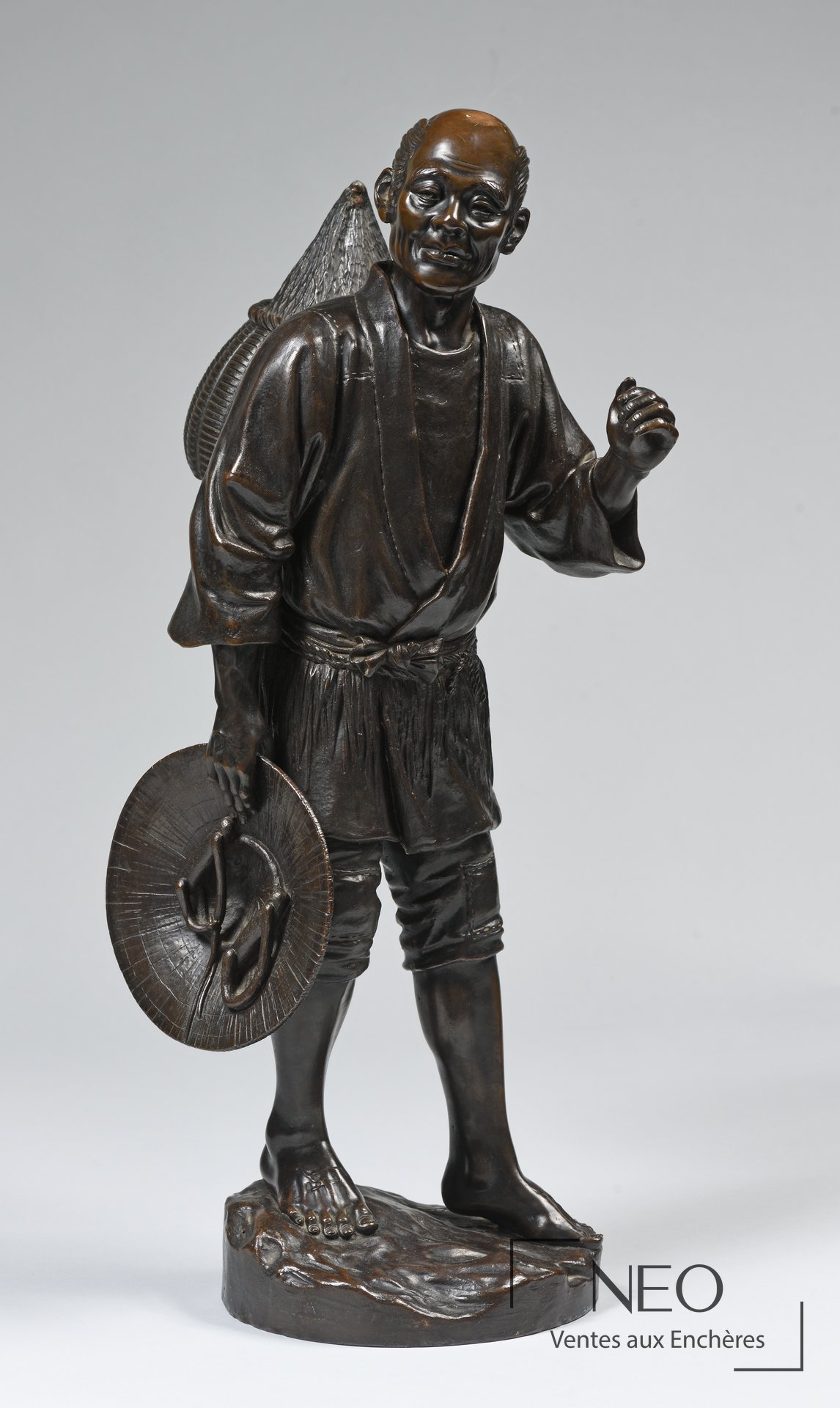 Okimono japonais en bronze représentant un paysan debout tenant un chapeau