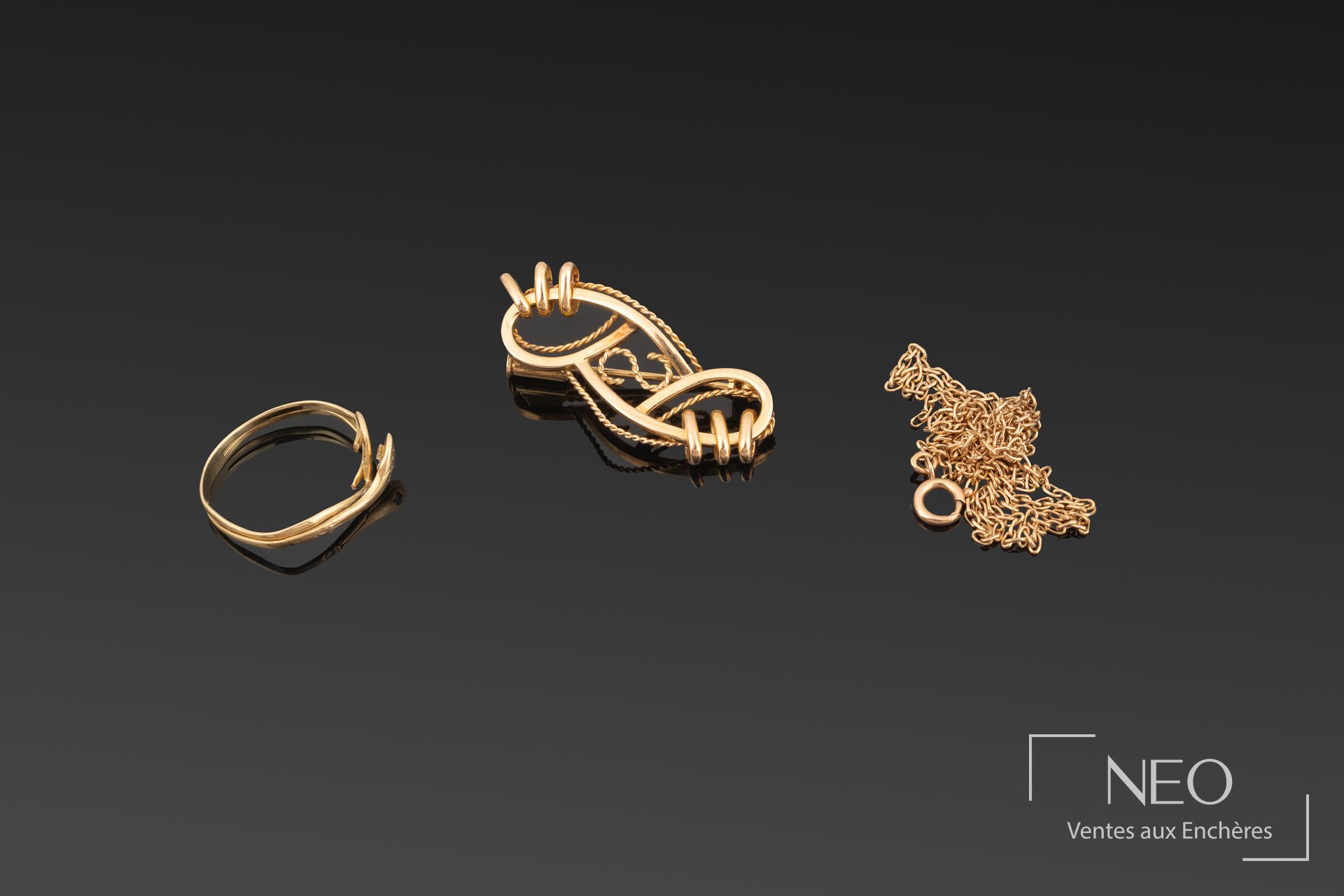 Trois bijoux en or jaune disposés sur fond noir : broche