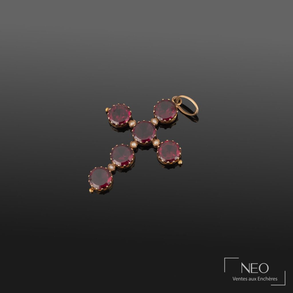 Pendentif croix latine en or jaune serti de grenats et de perles sur fond sombre