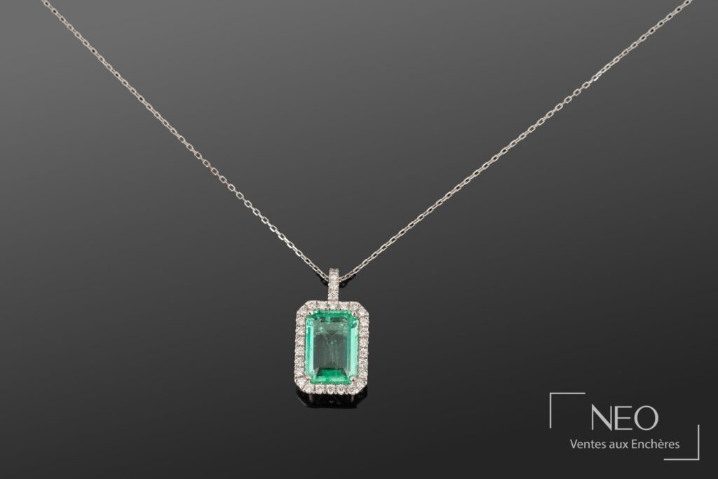Pendentif rectangulaire en or blanc avec émeraude centrale et entourage de diamants sur chaîne fine