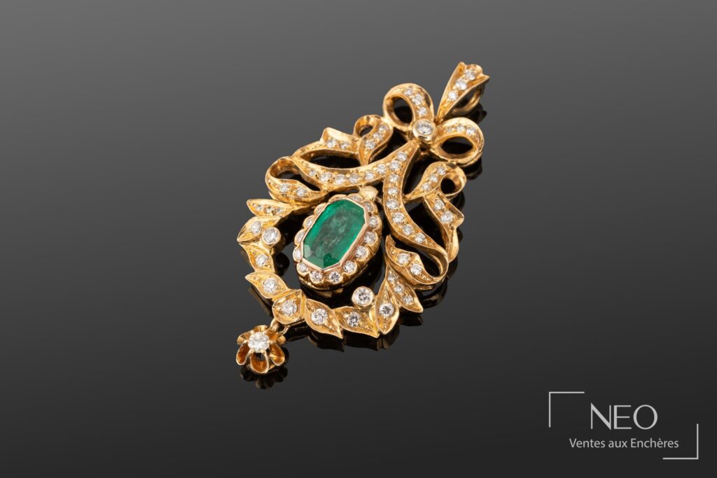 Pendentif en or jaune serti d’une émeraude centrale entourée de motifs de rubans brillants