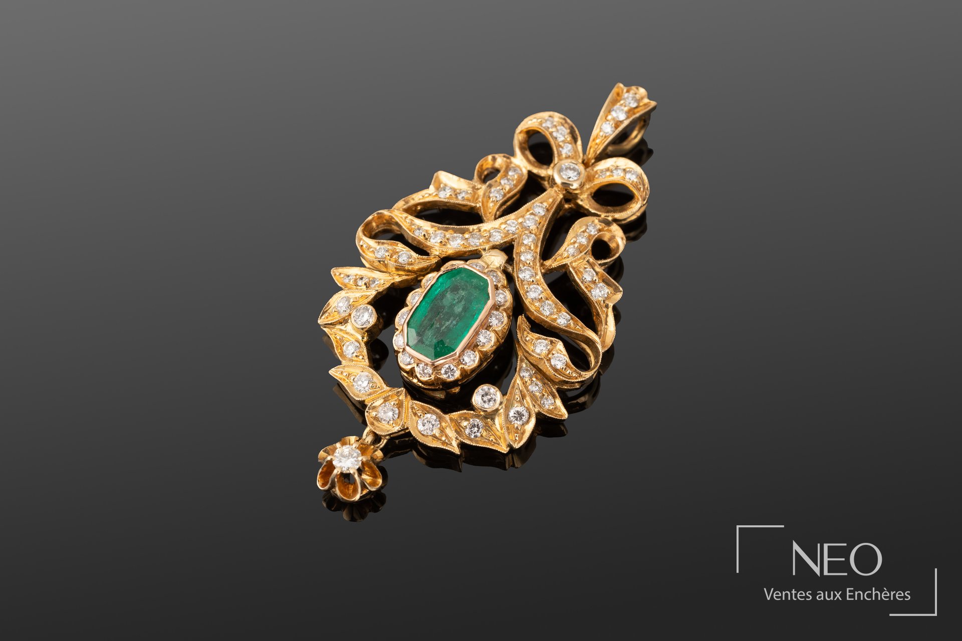 Pendentif en or jaune serti d’une émeraude centrale entourée de motifs de rubans brillants